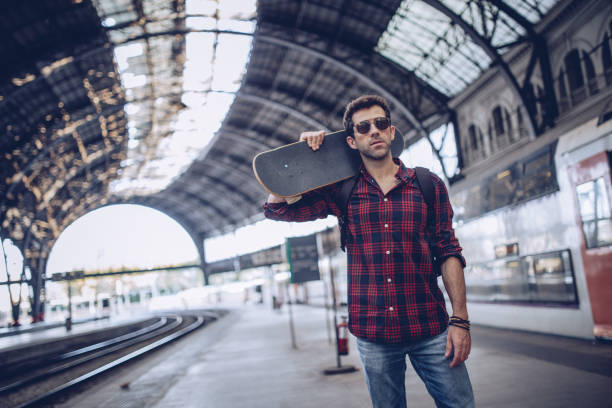 istock Hipster man with skateboard waiting a train 872159468
