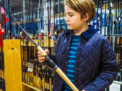A young angler in a fishing tackle shop looking at a new fishing rod.