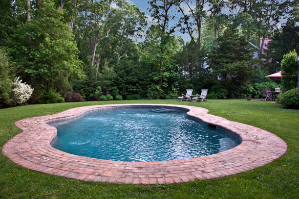 Backyard Pool A heated gunite pool surrounded by a brick patio showcases a beautifully landscaped backyard. the hamptons photos stock pictures, royalty-free photos & images