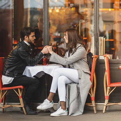 Young couple is sitting in a sidewalk cafe, holding hands. They are having a moment of closeness.