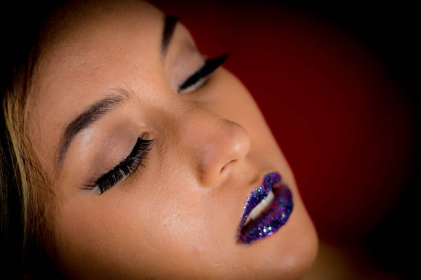 Fashion Lady Extreme Close-up Young lady pose for low key portrait with black background. In this headshot imager she has her eyes closed, the camera angle is from above and she is showing heavy and shinning makeup on face and lips. She is Latin, in her twenties. makeup look that dazzles stock pictures, royalty-free photos & images