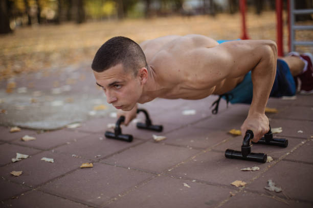 Push-ups outdoors Young man workout on exercise machine outdoors. Calisthenics training concept gripping bars stock pictures, royalty-free photos & images