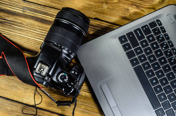 istock Modern DSLR camera and laptop on wooden table. Top view 872182048