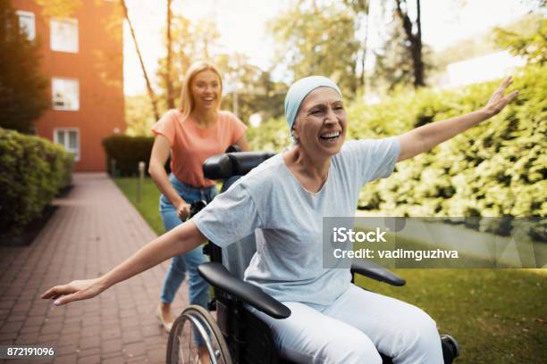 Eine Frau Mit Krebs Sitzt Im Rollstuhl Sie Geht Auf Der Straße Mit Ihrer Tochter Und Sie Herumtollen Stockfoto und mehr Bilder von Krebs - Tumor