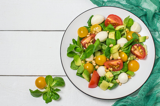 Fresh salad with mozzarella, tomatoes, sweet pepper, avocado and salad leaves. Served with vinaigrette sauce and siberian pine nuts. Concept of diet and healthy food. Green gauze napkin. Top view