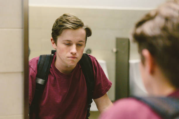 deprimiert teen schaut selbst im badezimmerspiegel - männlicher teenager stock-fotos und bilder