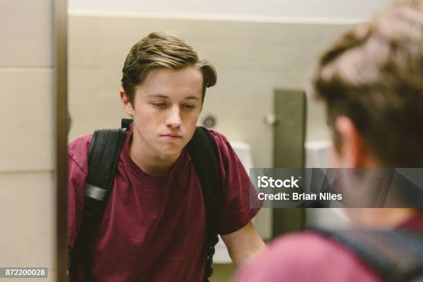 Depressed Teen Looks At Himself In Bathroom Mirror Stock Photo - Download Image Now - Teenager, Sadness, Teenage Boys