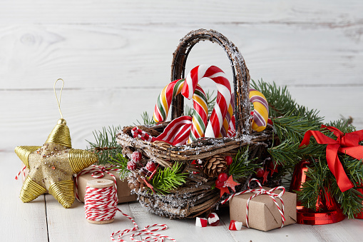 Christmas wicker basket with striped candy canes and gifts on white wooden table, festive decoration