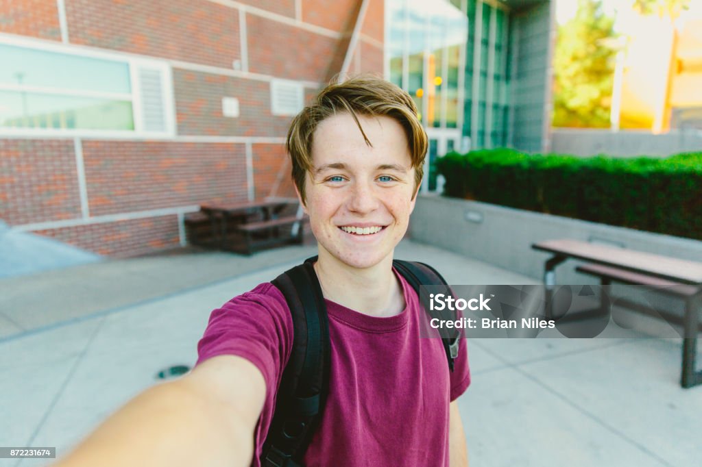 Cheerful Teen Boy With Backpack Taking Selfie Outside Teen student boy with blue eyes and brown hair wearing a backpack selfie with teeth smile Teenage Boys Stock Photo