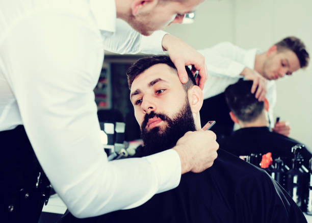 istock Adult man forming beard of client into shape 872250022