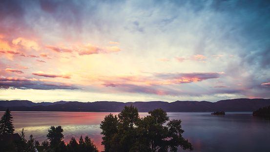 A brilliant colored autumn sky over Flathead Lake in Montana, USA. Mission mountain range is visible on the horizon across the lake. Color photograph shot in low light and long exposure after sunset. Color from the sky is reflected on the water's surface below. No people. Horizontal resolution.
