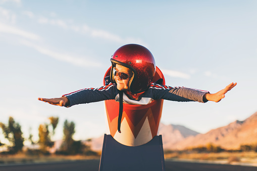 A young boy dressed in helmet and flight goggles sits ready for flight in a homemade cannon. His arms are outstretched and ready for take off as he is excited to explore new heights. Image taken on a rural road in Utah, USA.