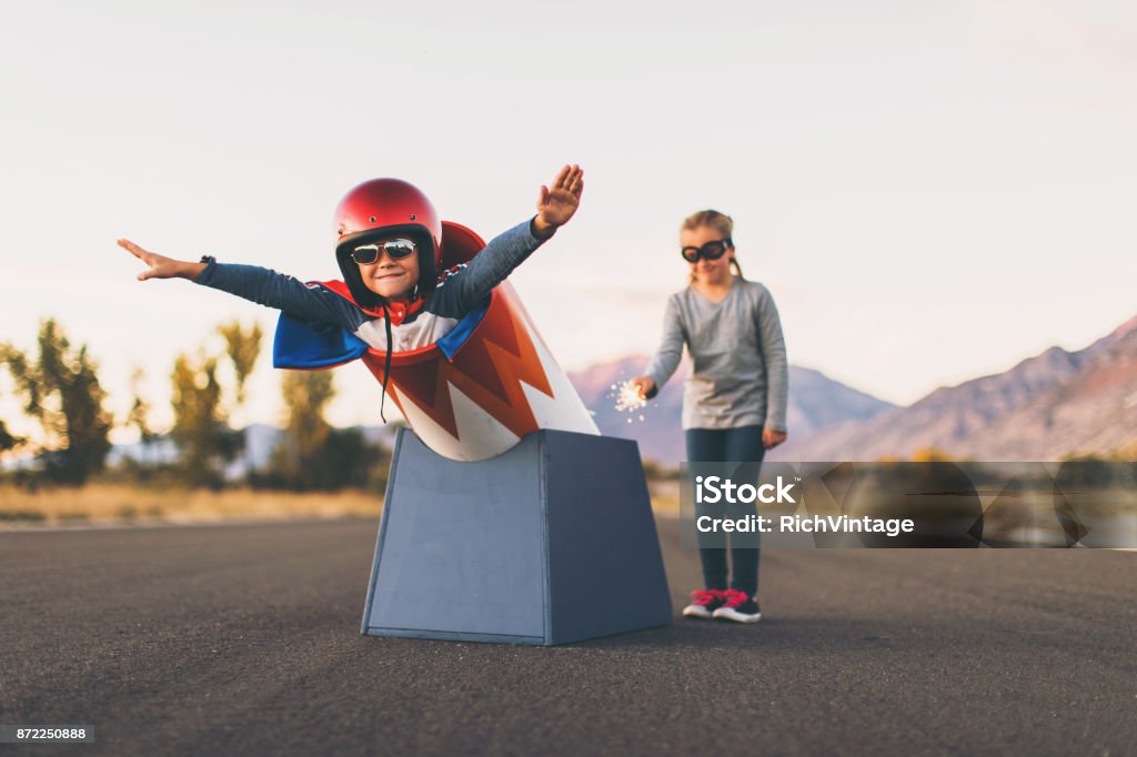 Young Stunt Boy and Human Cannon Ball A young boy dressed in helmet and flight goggles sits ready for flight in a homemade cannon while his sister is ready to light the fuse. His arms are outstretched and ready for take off as he is excited to explore new heights. Image taken on a rural road in Utah, USA. Anticipation Stock Photo