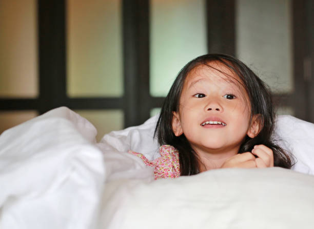 istock Little asian girl lying under blanket on the bed. 872268064