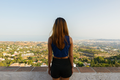 Back view of young Asian tourist woman enjoying the beautiful scenery of the mountains of Mijas village in Costa Del Sol, Málaga, Spain