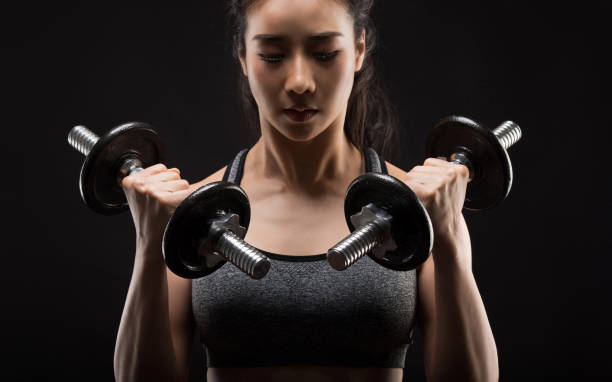 Beautiful girl exercising squatting with dumbbells on black. stock photo