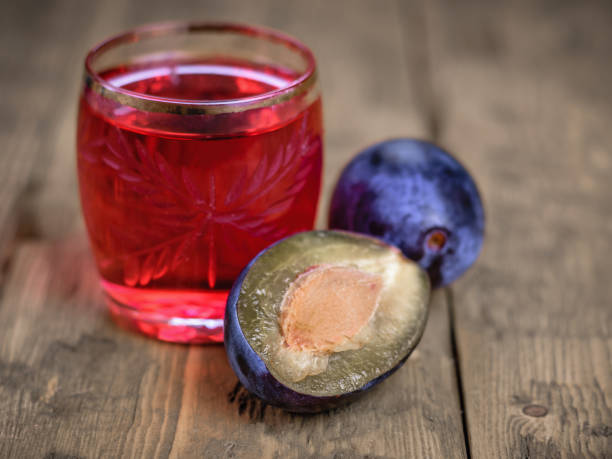 two ripe plums and a glass of fresh homemade plum aperitif on a wooden rustic table. - plum fruit organic food and drink imagens e fotografias de stock