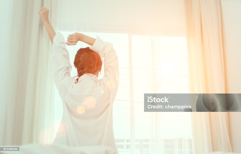 Young woman wake up in the morning and sitting on bed at window door side relaxing in holiday with sunlight, back view Sleeping Stock Photo