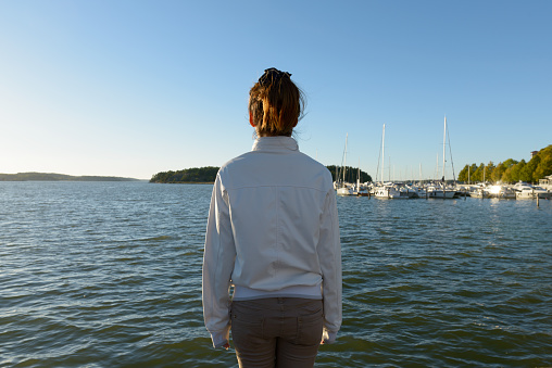 Back view of young woman standing on end of pier in Finland