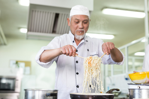 Mature asian chef preparing nudles in restaurant.