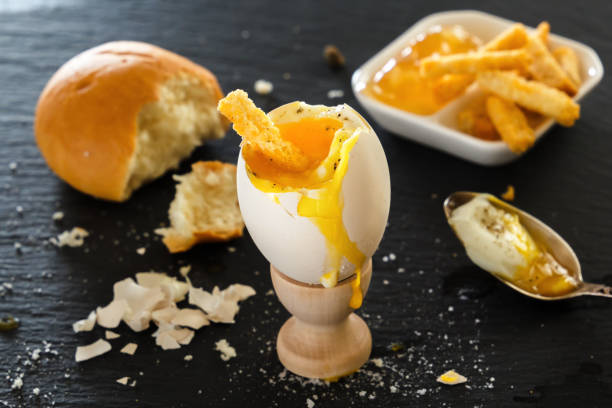 istock Soft boiled egg in a wooden egg cup, a piece of bread, toast-crackers. eggshell on a black table 872298066