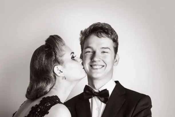 Photo of Elegant girl kisses a happy young man on the cheek