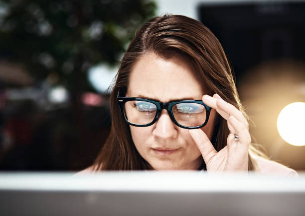 Serious woman working late peers at PC over her spectacles