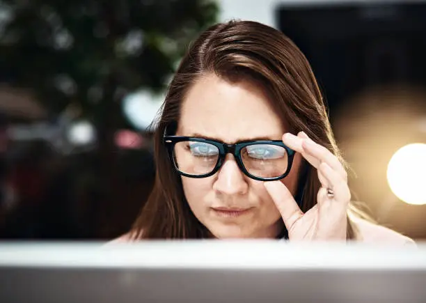 Photo of Serious woman working late peers at PC over her spectacles