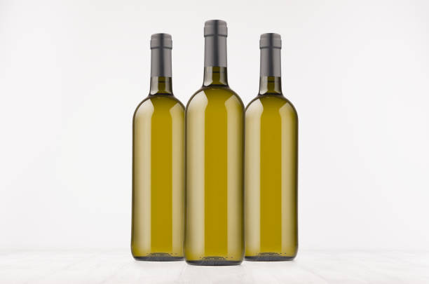 istock Three green wine bottles with white wine on white wooden board, mock up. 872324830