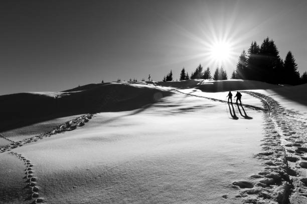 два лыжника, идущих к вершине креста. солнечные лучи и подсветка. - winter sunset stream snow стоковые фото и изображения