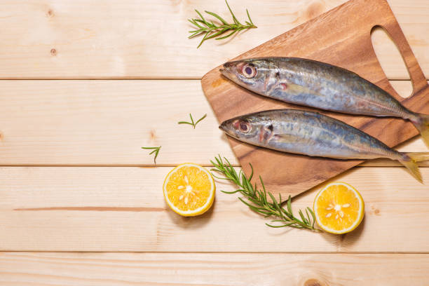 istock Fish dish cooking with various ingredients. Fresh raw fish decorated with lemon slices and herbs on wooden table. 872352318