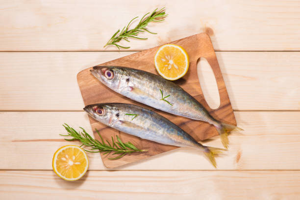 istock Fish dish cooking with various ingredients. Fresh raw fish decorated with lemon slices and herbs on wooden table. 872352320