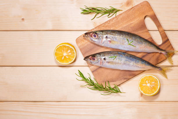 istock Fish dish cooking with various ingredients. Fresh raw fish decorated with lemon slices and herbs on wooden table. 872352322