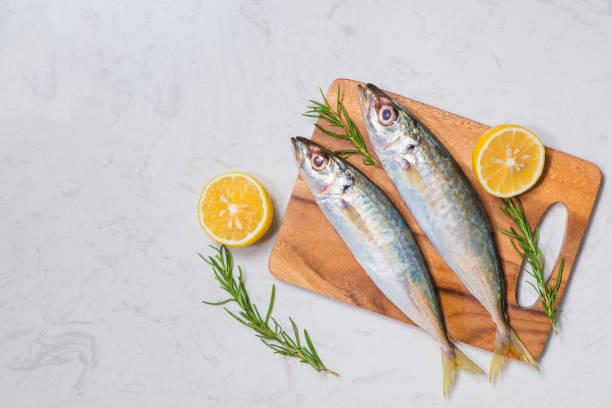 istock Fish dish cooking with various ingredients. Fresh raw fish decorated with lemon slices and herbs on wooden table. 872352634