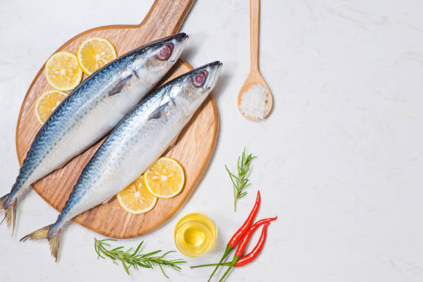 istock Fish dish cooking with various ingredients. Fresh raw fish decorated with lemon slices and herbs on wooden table. 872352636