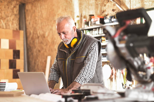 istock Mature carpenter in his workshop on laptop 872353304