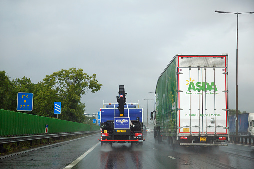 London, UK: July 12, 2016: Freight transportation on UK roads. Trucks drive on the M4 motorway in hazardous weather conditions with limited visibility creating water spray
