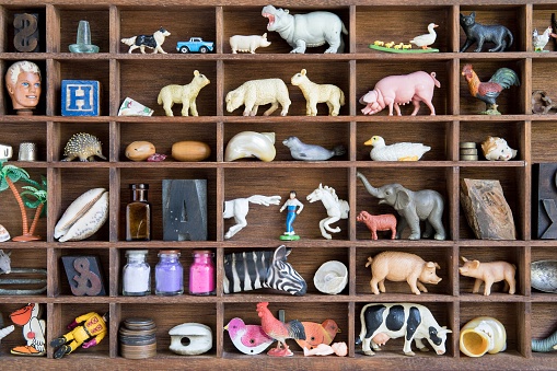 A collection of found objects including toy farm and zoo animals, old cars, seashells, bottles, Cupid dolls,