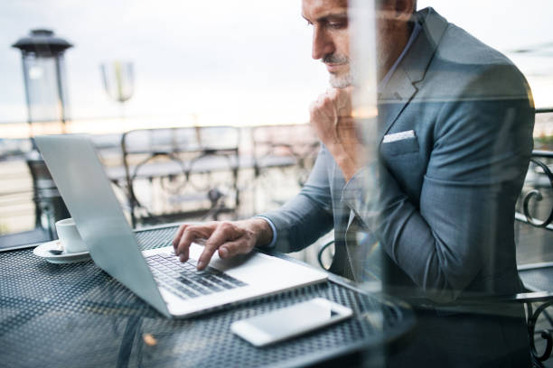 istock Mature businessman with laptop outside a cafe. 872367930