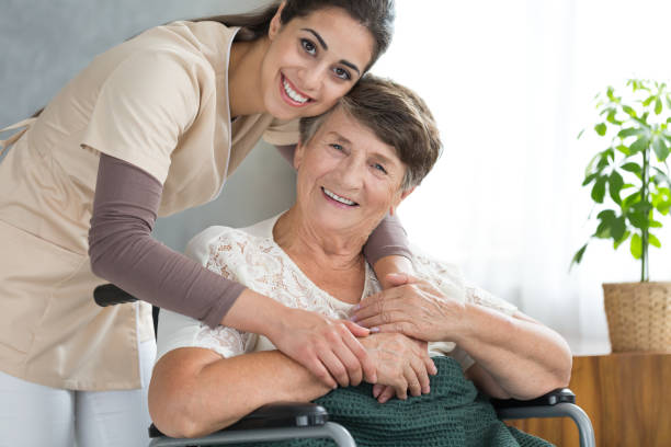 Pretty caregiver hugging disabled senior Pretty caregiver in uniform hugging disabled senior woman during visit at home parkinsons disease photos stock pictures, royalty-free photos & images