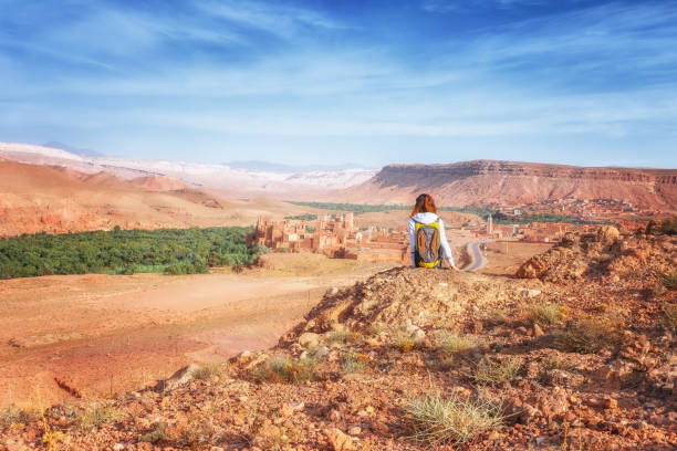 молодая женщина смотрит на укрепленный город. глауи касба из telouet kasbah или ksar в марокко вид сверху. девушка-путешественница сидит на скале и с - ksar стоковые фото и изображения