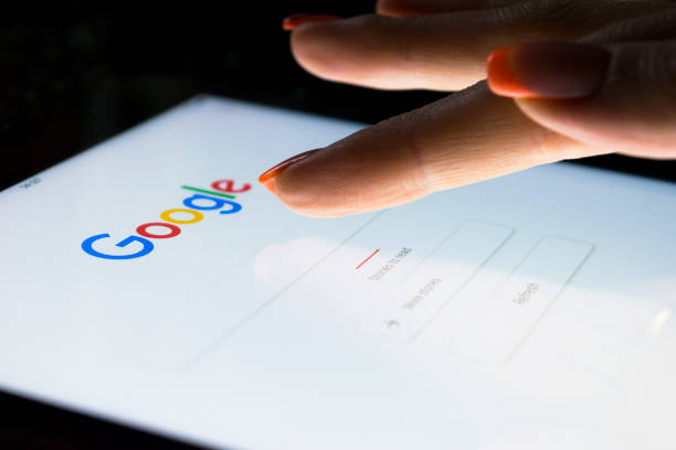 A woman's hand is touching screen on tablet computer iPad Pro at night for searching on Google search engine. Google is the most popular Internet search engine in the world. stock photo