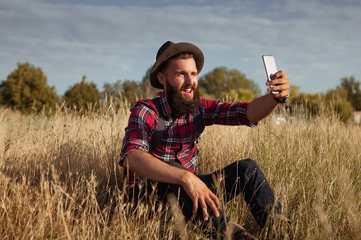 Cheerful man winking and taking selfie with smartphone on field.