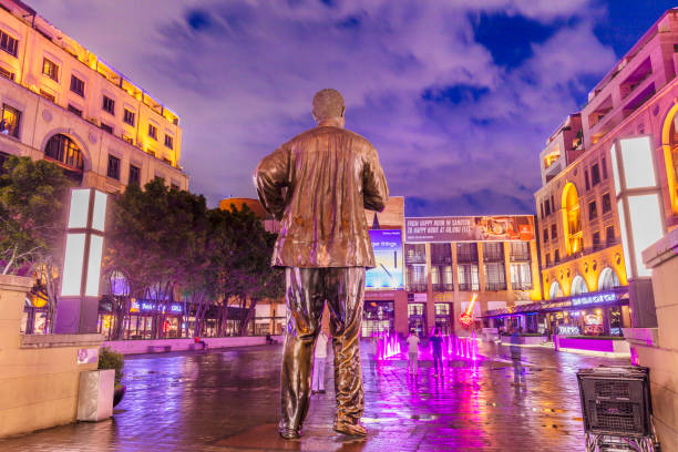 Nelson Mandela Square in the evening with a water feature and Mandela statue seen from behind facing Sandton Library accross the square with surrounding restaurants.