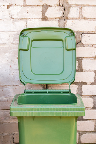 Opened empty dirty green recycle bin near the brick wall