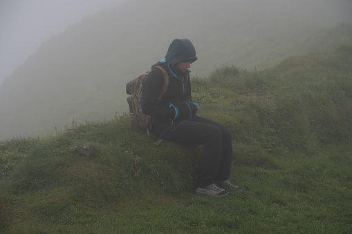 tired explorative girl after hiking on the cliffs of the Faroe Islands in Mykines with foggy weather.