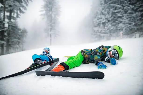 Photo of Little skiers lying on slope after crashing