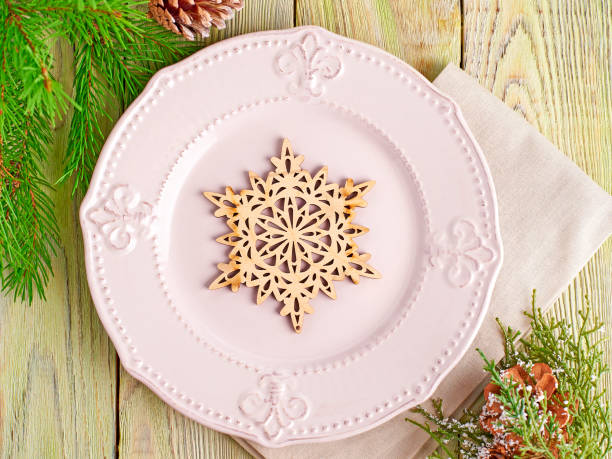 istock Christmas table setting in rustic style. Wooden snowflake on a pink plate with a cloth napkin on background light wooden boards. 872441726