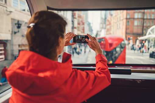 Young woman traveling in bus and taking photos of the city