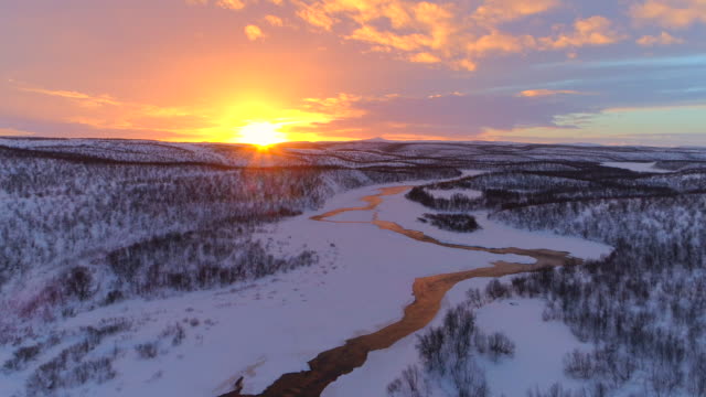 AERIAL: Meandering river flowing through gorgeous hilly winter landscape Lapland